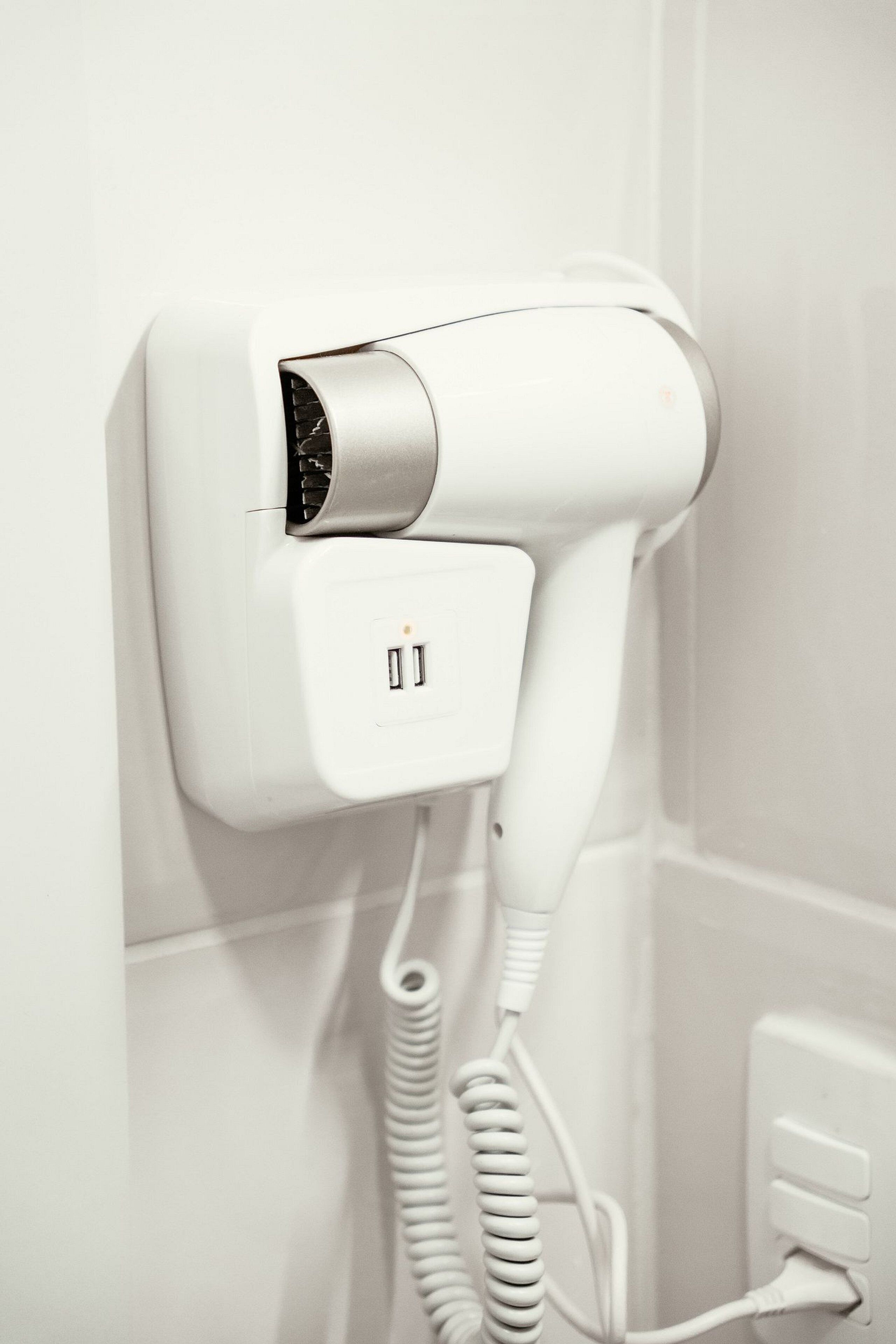 Een haardroger bevestigd aan een muur, met een opgerolde snoer en een stopcontact.