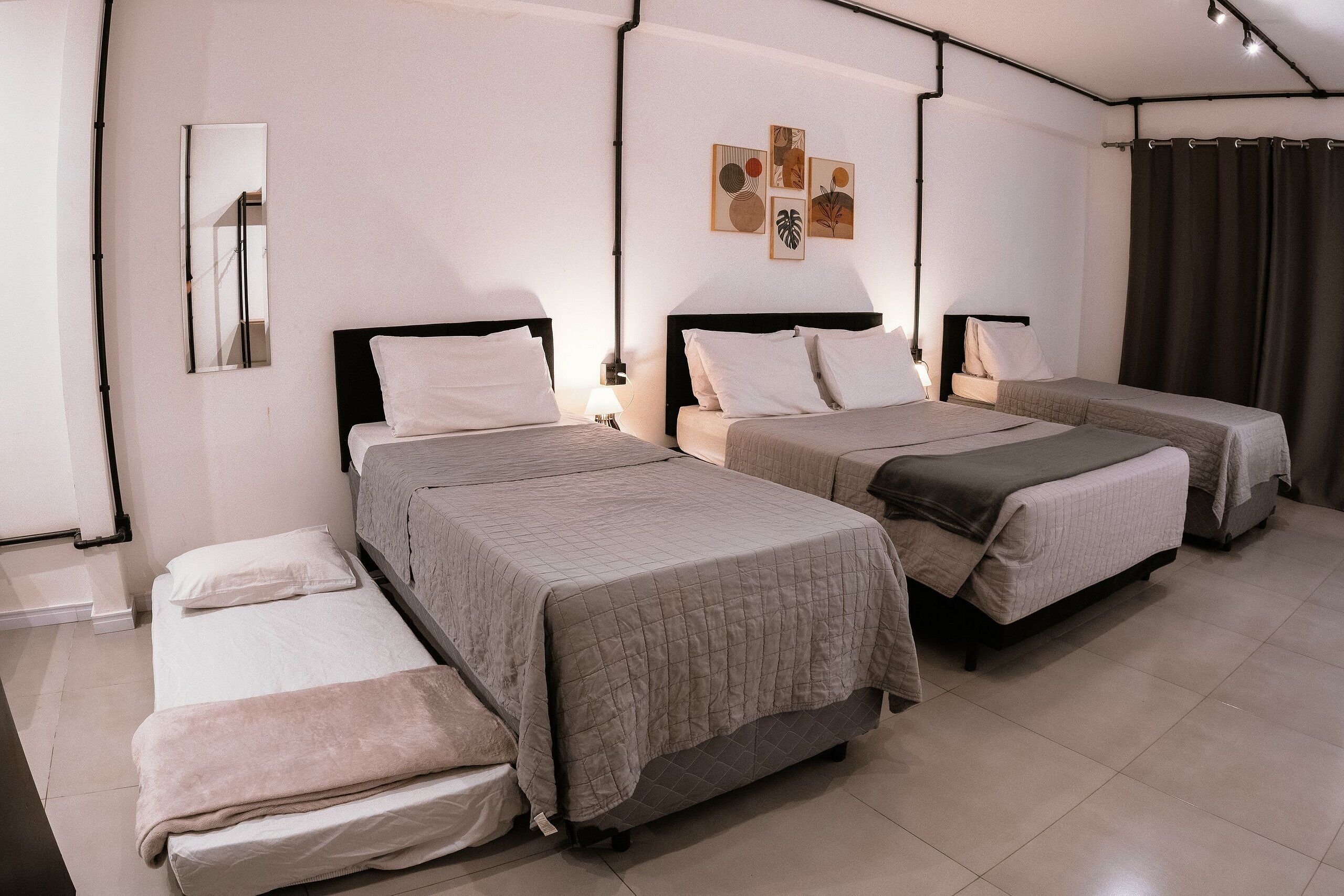 A hotel room with three beds, a mirror, artwork on the wall, and a curtain.