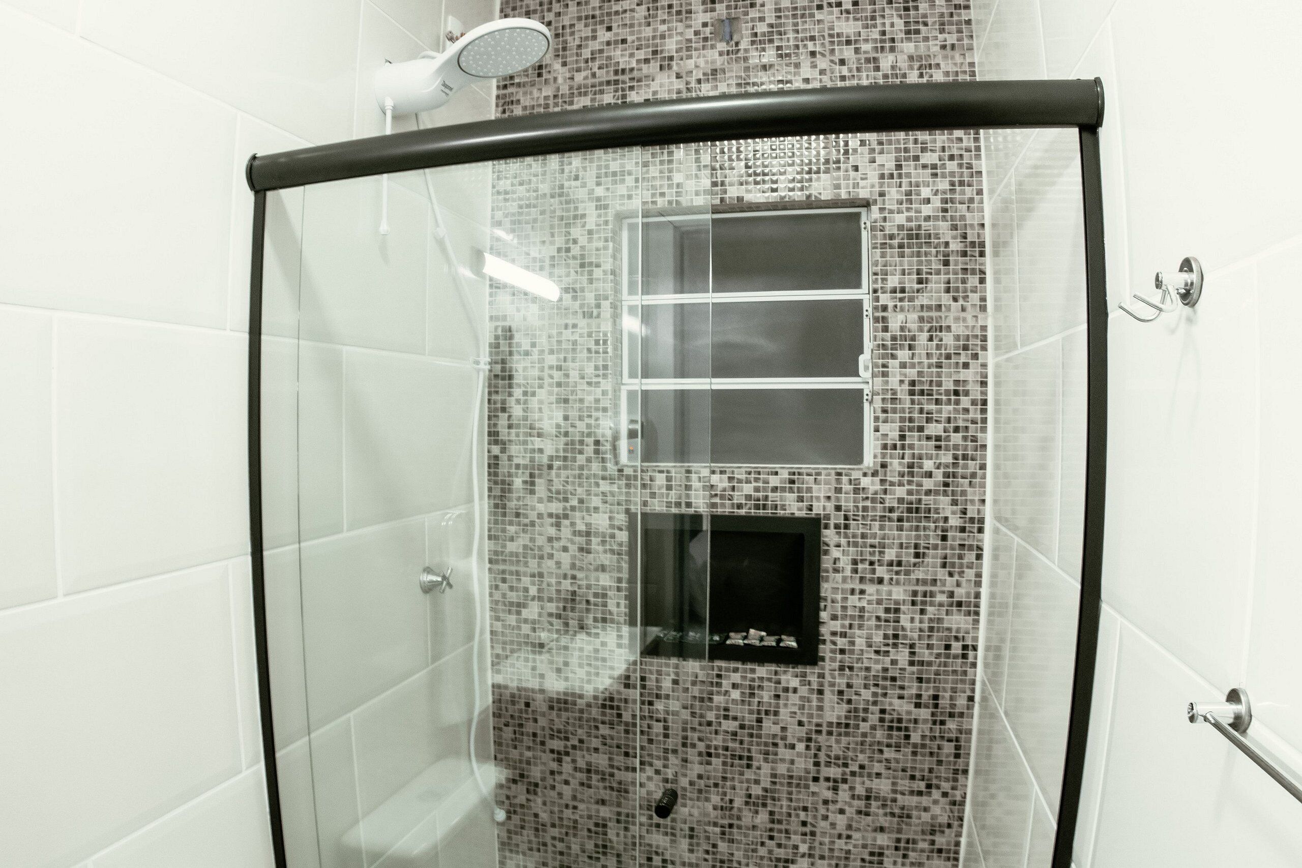 Boxe de vidro com parede em mosaico de azulejos, chuveiro manual e porta-toalhas.