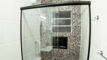 Boxe de vidro com parede em mosaico de azulejos, chuveiro manual e porta-toalhas.