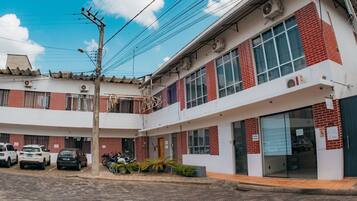 Un edificio de varios pisos con estacionamiento, un área de estar al aire libre techada y una fachada con puerta de vidrio.