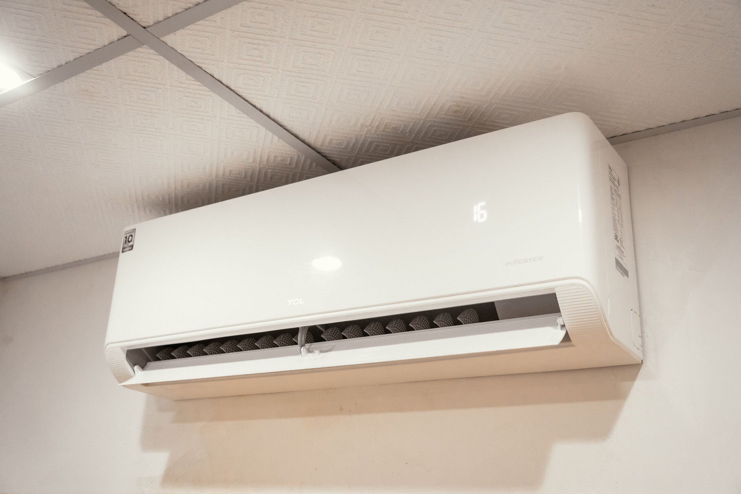 A white air conditioner mounted on a ceiling with a visible brand logo and model number.