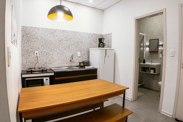 A compact kitchen with a wooden table, a coffee machine, and a microwave. - VILLA BILAC 04 (Blumenau)
