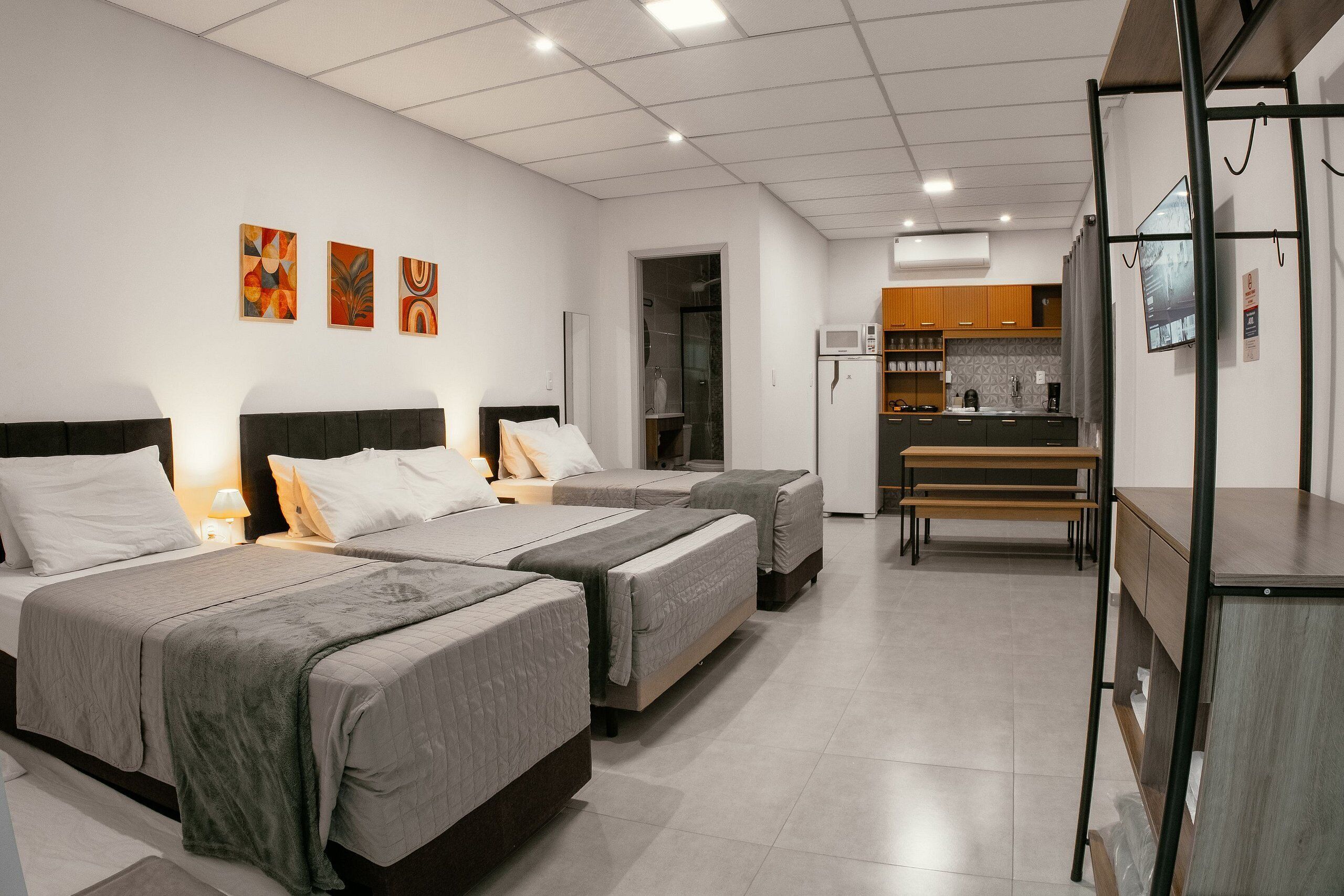A hotel room with two beds, a kitchenette, and a bathroom.