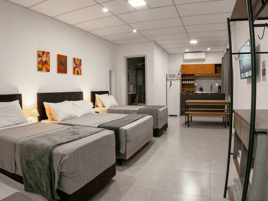 Quarto de hotel com duas camas, uma cozinha compacta e um banheiro.