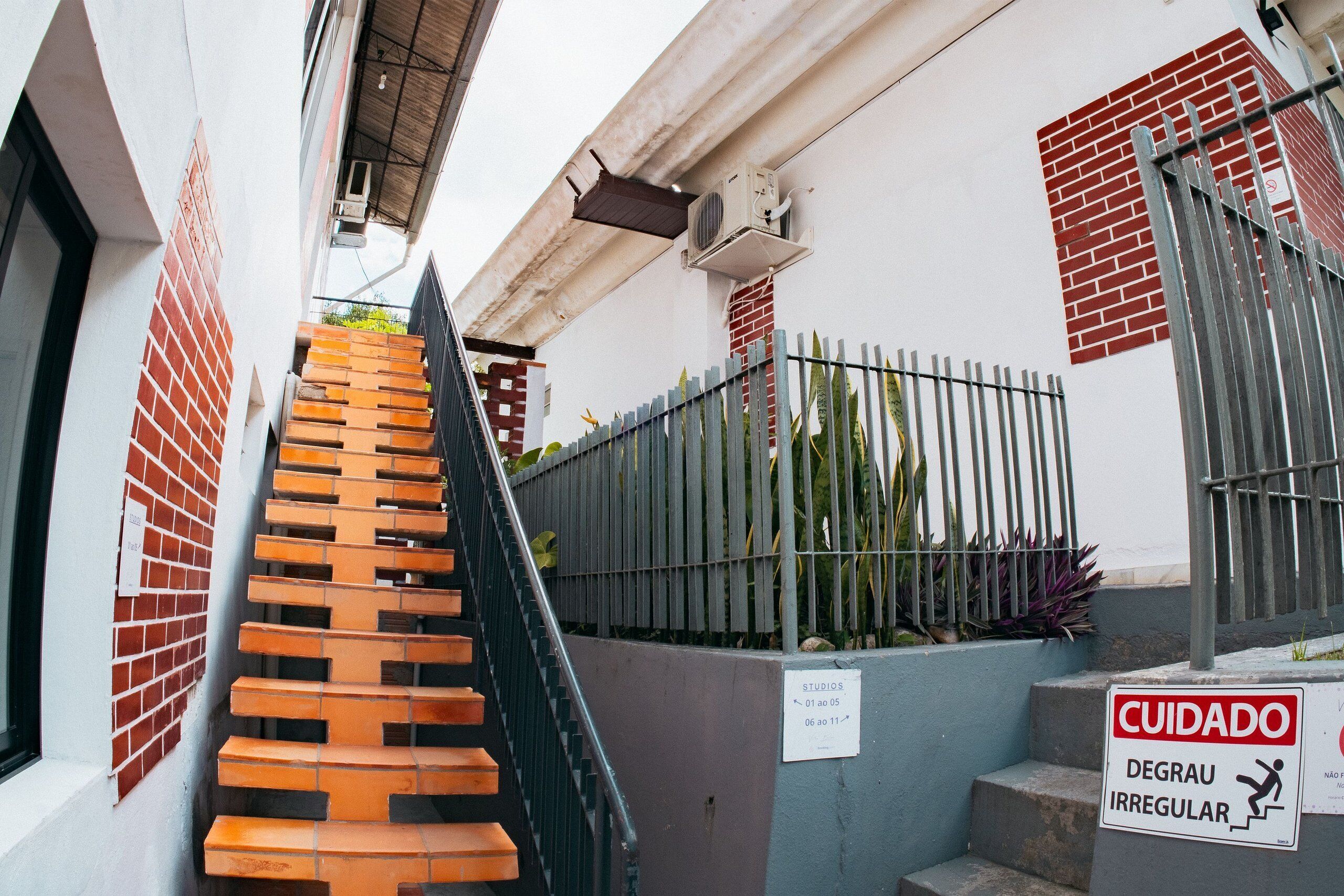 Una escalera que lleva a un edificio con una cerca metálica y un letrero que indica escalones irregulares.