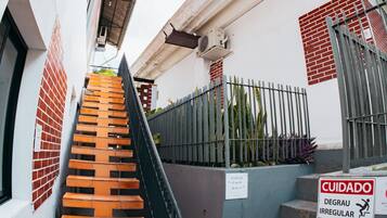 Una escalera que lleva a un edificio con una cerca metálica y un letrero que indica escalones irregulares.