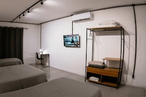 Habitación con dos camas, un escritorio con silla, televisor montado en la pared y una litera con espacio de almacenamiento.