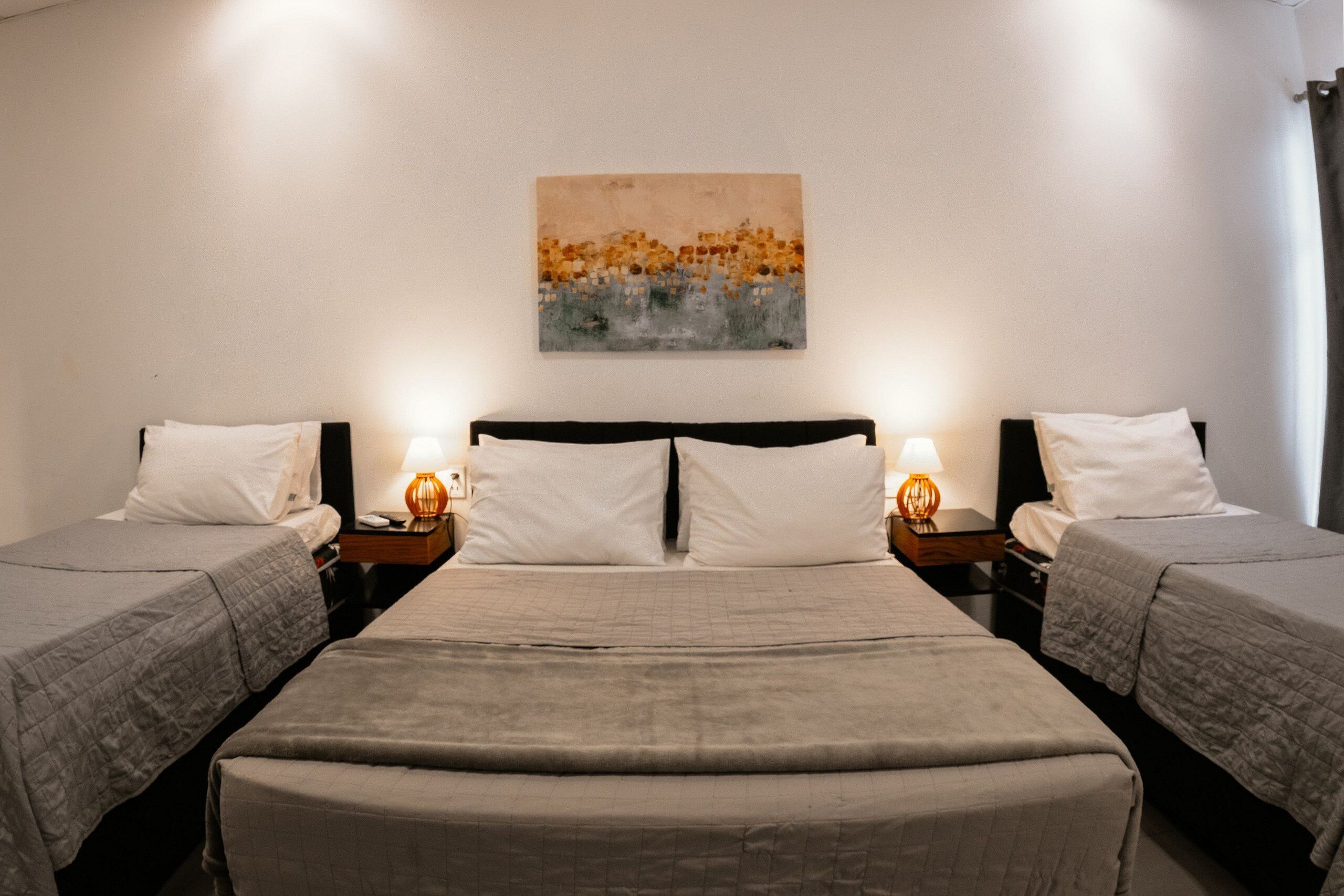 Quarto duplo com duas camas, uma mesa de cabeceira com abajur e um quadro na parede.