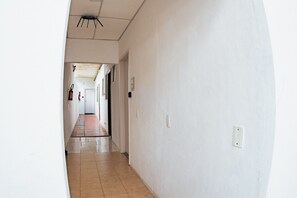 Un pasillo con piso de baldosas, paredes blancas y un artefacto de iluminación en el techo.