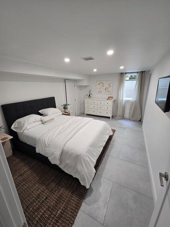 A modern bedroom with a bed, dresser, and artwork on the wall. - Beautiful East Hampton Retreat (East Hampton)