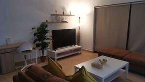 Ein Wohnzimmer mit Fernseher, Sofa, Couchtisch und einer Pflanze.