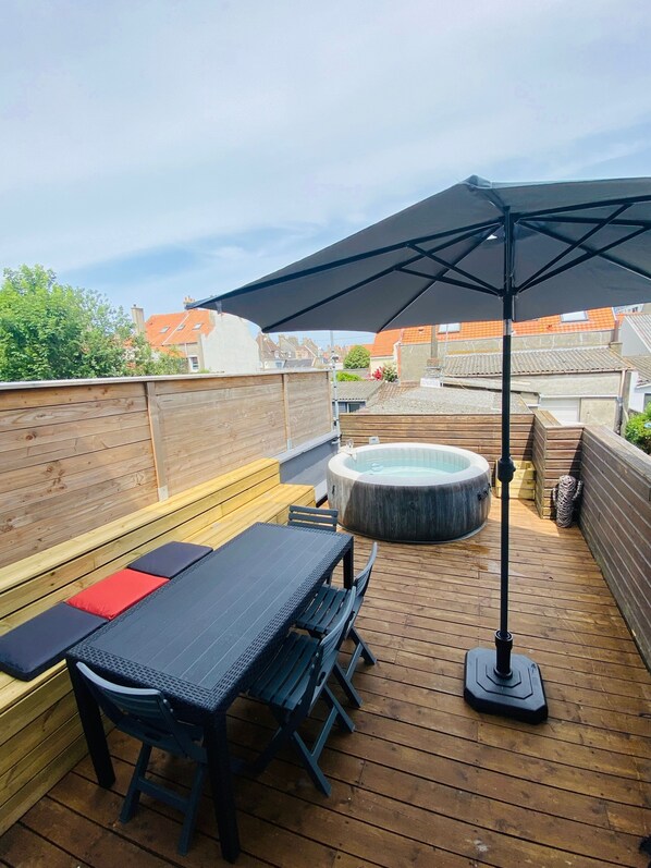 A wooden deck with a hot tub, a table, and benches.