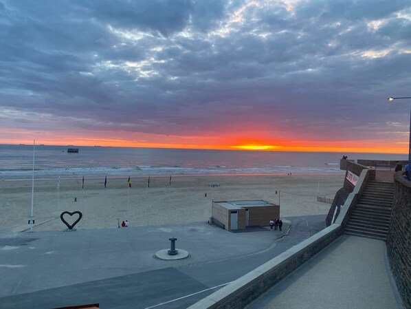 A beach with a sunset, a heart-shaped sculpture, and a small building.