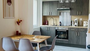Een moderne keuken met grijze kastjes, een roestvrijstalen afzuigkap en een inbouwoven. Er is een eethoek met een houten tafel en grijze stoelen.
