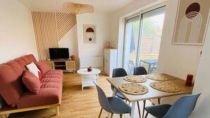 Een moderne woonkamer met een rode bank, een eettafel met vier stoelen, een televisie en een groot raam.