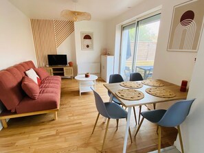 A modern living room with a red sofa, a dining table with four chairs, a TV, and a large window.