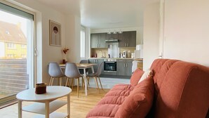 Een moderne woonkamer met een bank, een eettafel met stoelen en een keuken op de achtergrond.
