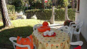 Un área de comedor al aire libre con una mesa dispuesta para cuatro personas, rodeada de sillas blancas, y una señal de parada al fondo.