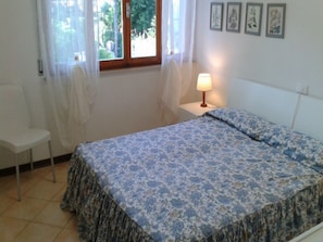 Una camera da letto con un letto, una sedia, un comodino con una lampada e una finestra con tende.