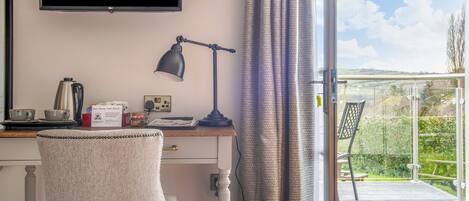 Een kamer met een bureau, een stoel, een televisie, een lamp en uitzicht op de omgeving.