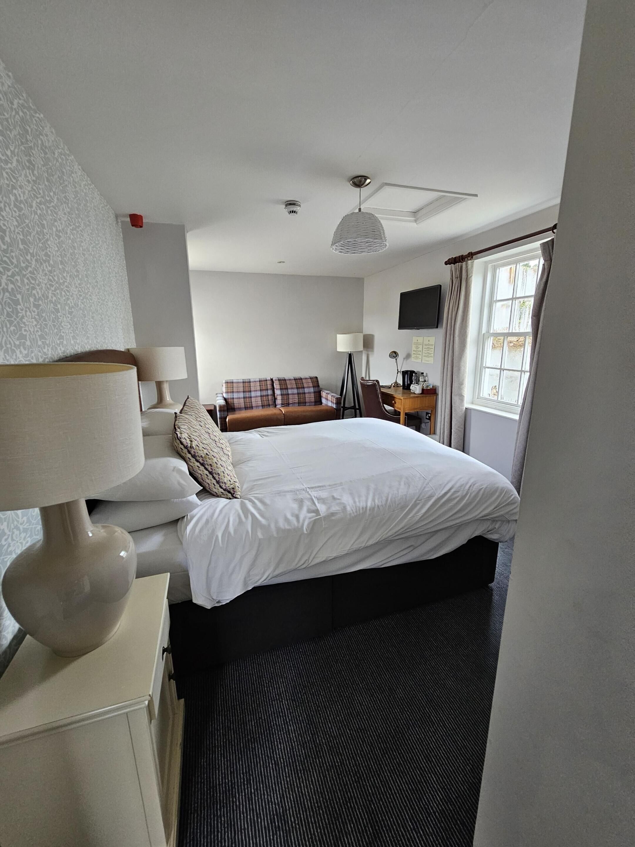 A hotel room with a bed, a desk, a chair, a lamp, a television, and a window with curtains.