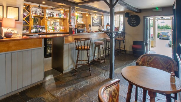 A bar area with wooden bar stools, a counter with bottles, and a view of the outside. - Cockhaven Arms (Teignmouth)