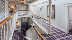 A staircase with a checkered floor and white railings, leading to an upper level with a chandelier and framed pictures. - Cockhaven Arms (Teignmouth)