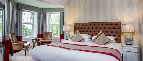 A hotel room with a large bed, a sitting area with chairs, a small table, and a window with curtains.