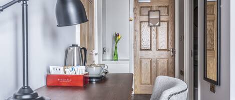 Uma mesa de jantar de madeira com uma luminária de mesa preta, uma caixa vermelha com a etiqueta "BIRCHALL" e um vaso verde com flores.