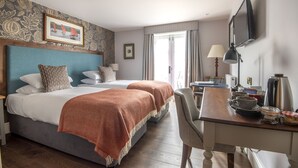 A hotel room with two beds, a desk, a chair, a television, and a window with curtains. - Cockhaven Arms (Teignmouth)