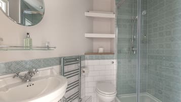 Un baño con lavamanos blanco, espejo, inodoro, ducha con mampara de vidrio y baldosas con diseño.