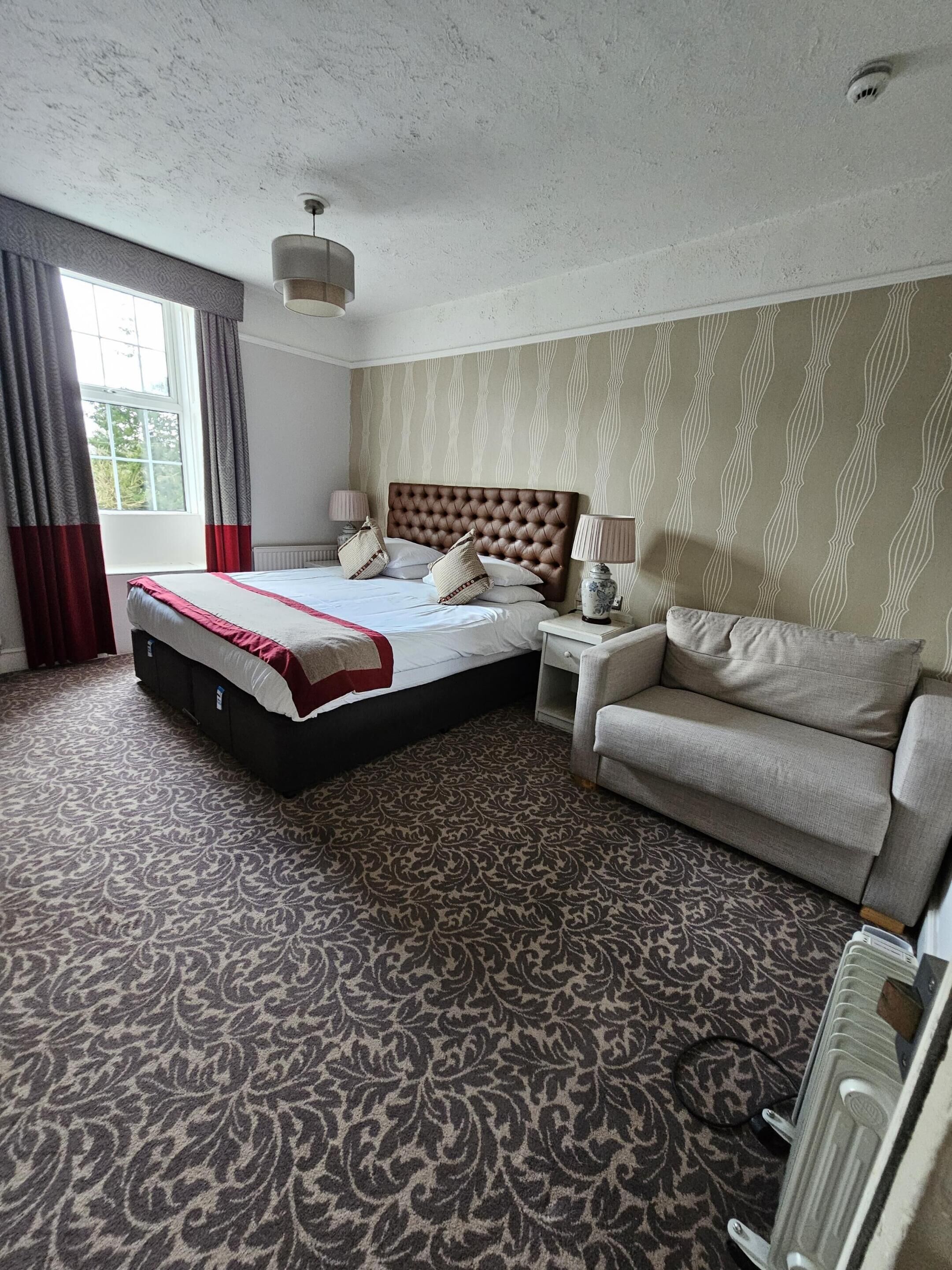 Een hotelkamer met een groot bed, een bank, een nachtkastje en een raam met gordijnen.