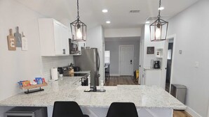A modern kitchen with white cabinets, granite countertops, two black bar stools, and pendant lighting. - ~ Houston Heights 4-plex with patio ~ (Houston)
