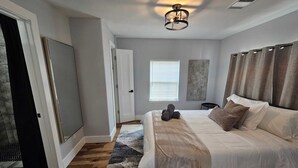 A bedroom with a large bed, a ceiling fan, a window with blinds, and a door. - ~ Houston Heights 4-plex with patio ~ (Houston)