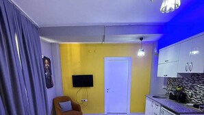 Un espacio habitable compacto con sofá, mesa de centro, televisor y kitchenette.