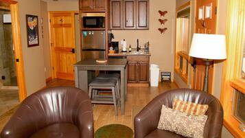 A kitchen with wooden cabinets, a microwave, and a refrigerator. There are two leather chairs and a small table.