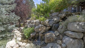 A natural stone waterfall cascading over rocks, surrounded by various trees and shrubs. - Luxury - 6000sqft- Sleeps 22+ Basketball, Billiards, Theater, Game, PrincessRoom (Layton)