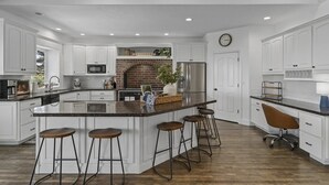 A spacious kitchen with white cabinetry, a central island with stools, a brick arch, and modern appliances. - Luxury - 6000sqft- Sleeps 22+ Basketball, Billiards, Theater, Game, PrincessRoom (Layton)