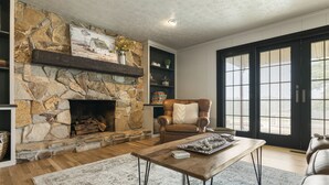 A cozy living room with a stone fireplace, leather armchair, and a large window with blinds. - Amazing views, hot tub/outdoor fireplace, countryside, farm (Navarre)