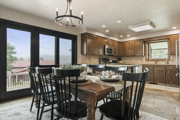 A dining area with a wooden table and chairs, a chandelier, and a view of the outdoors. - Amazing views, hot tub/outdoor fireplace, countryside, farm (Navarre)