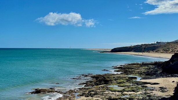 Un paysage côtier caractérisé par un ciel dégagé, une mer calme, une côte rocheuse et une plage de sable.