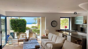 Un salon moderne avec un canapé, une table basse et une vue sur la mer grâce à de grandes fenêtres.