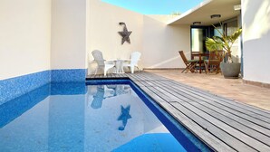 Une piscine avec une terrasse en bois, des chaises blanches et une décoration en forme d’étoile sur le mur.