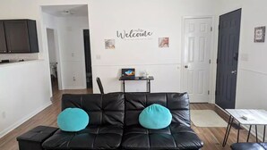 A living room with a black leather sofa, two teal cushions, a small table, and a door.