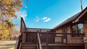 A wooden staircase leading to a covered deck area with a brick building in the background.