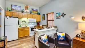 A compact kitchen with wooden cabinets, a refrigerator, microwave, and a dining area with a table and chairs. - Angel Fire Studio w/ Fireplace, Walk to Resort! (Angel Fire)