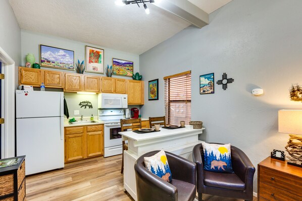 A compact kitchen with wooden cabinets, a refrigerator, microwave, and a dining area with a table and chairs.