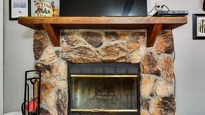 A stone fireplace with a wooden mantel shelf, a television mounted above it, and a power outlet on the wall. - Angel Fire Studio w/ Fireplace, Walk to Resort! (Angel Fire)