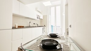 Une cuisine moderne avec des meubles blancs, une table à plateau en verre et une vue sur un balcon.